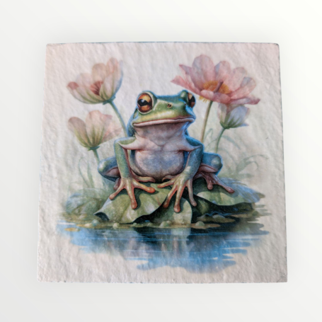 A green frog sits on a lily pad surrounded by pink flowers and water.