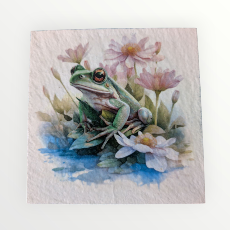A green frog sitting among pink flowers and water lilies by a pond.